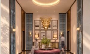 Residential lift lobby at MABA Suitez with a round upholstered seat, sculptural gold chandelier, gallery wall and blue louvred doors.