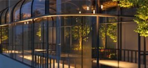 Loft Lounge at MABA Suitez with a curved glass exterior, sheltered seating, planted trees and warm evening lighting.