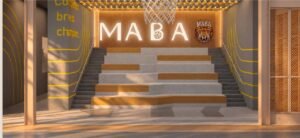 MABA Court seating area at MABA Suitez featuring stepped benches, a hanging basketball net, illuminated MABA sign and wall graphics